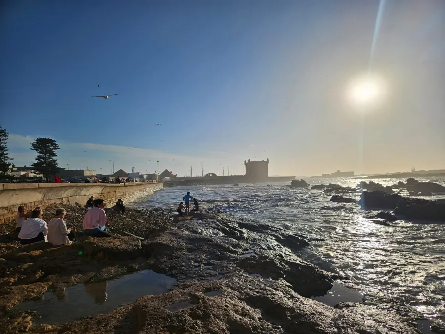 Late sun over rocks and waves on the Atlantic coast, a fortress tower in the distance
