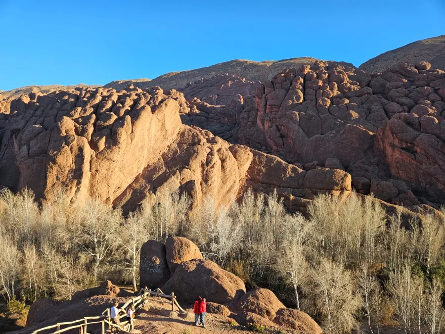 Rounded red rock formations above dry grasses under a clear blue sky