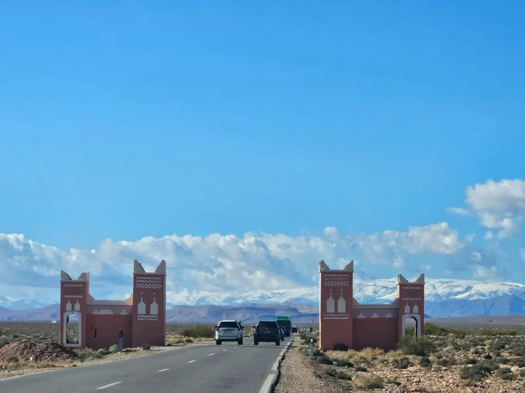 A straight road through a red town gate, with snow on the mountains in the distance