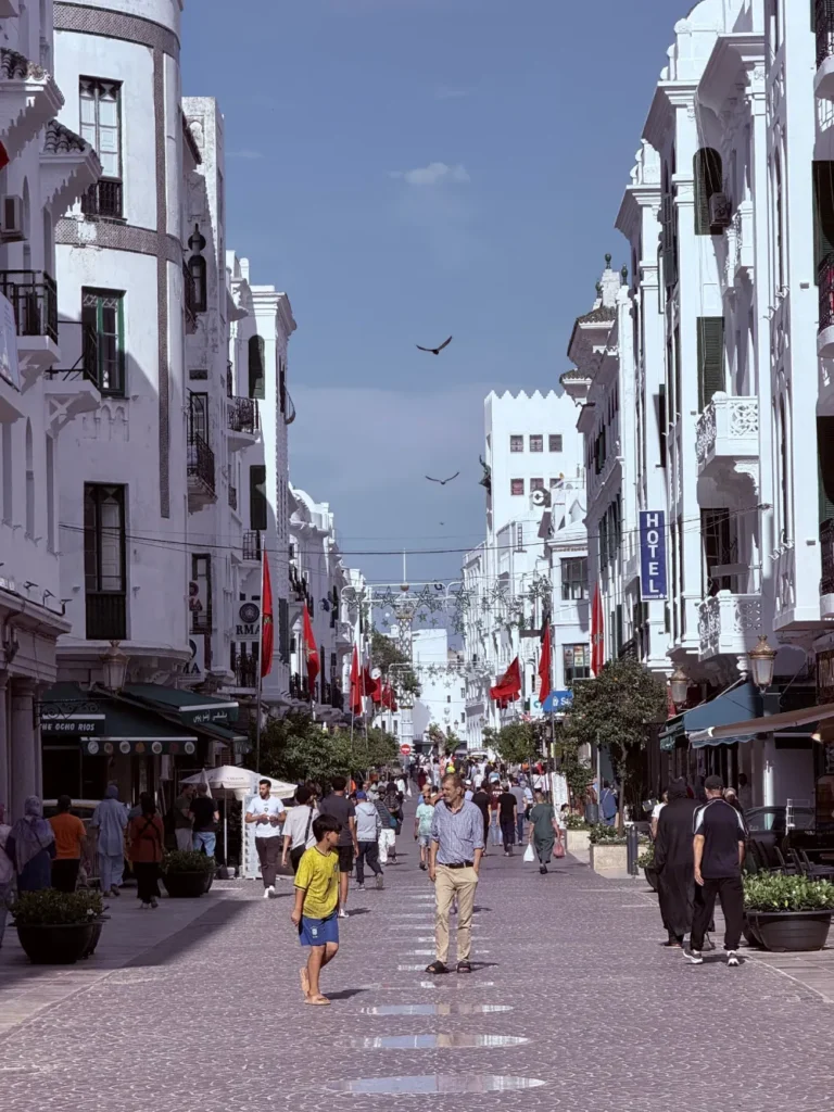 A sunny pedestrian street in Tangier lined with white buildings and Moroccan flags